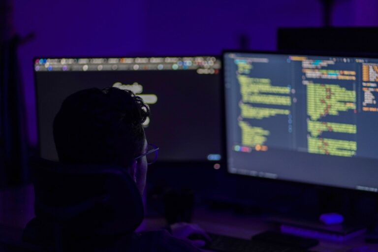 Man sitting in front of 2 monitors looking at code