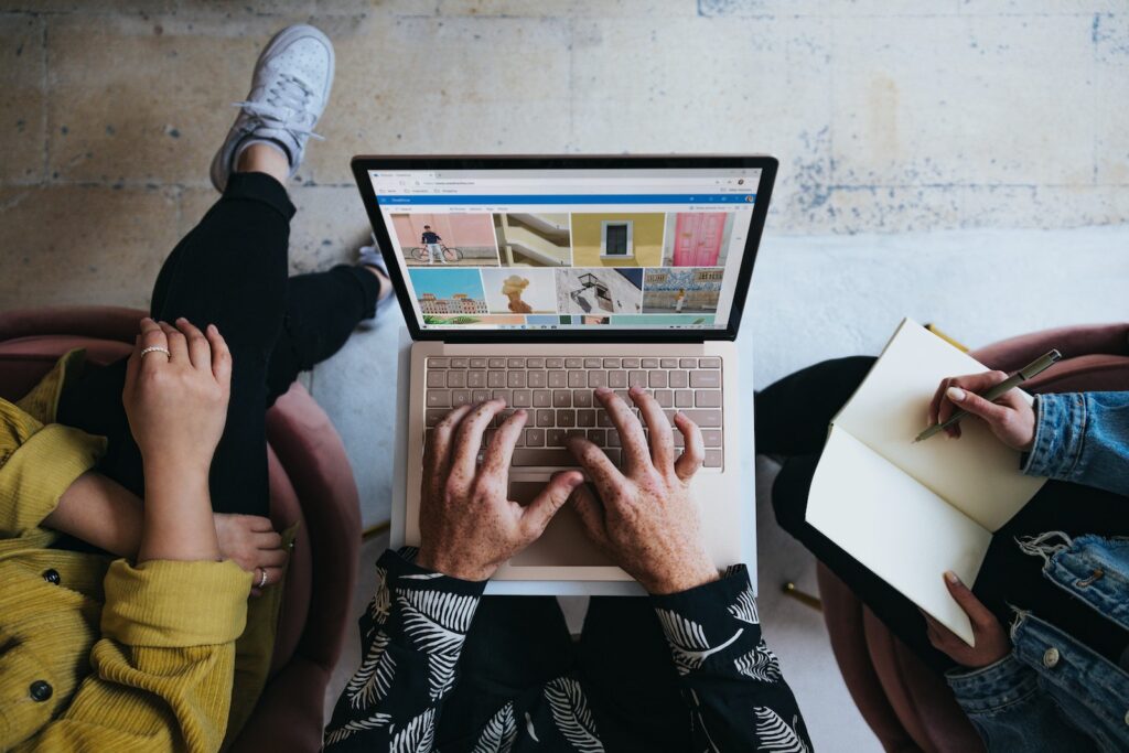 3 Personen sitzend auf einer Bank. Eine Person tippt etwas auf ihrem Laptop